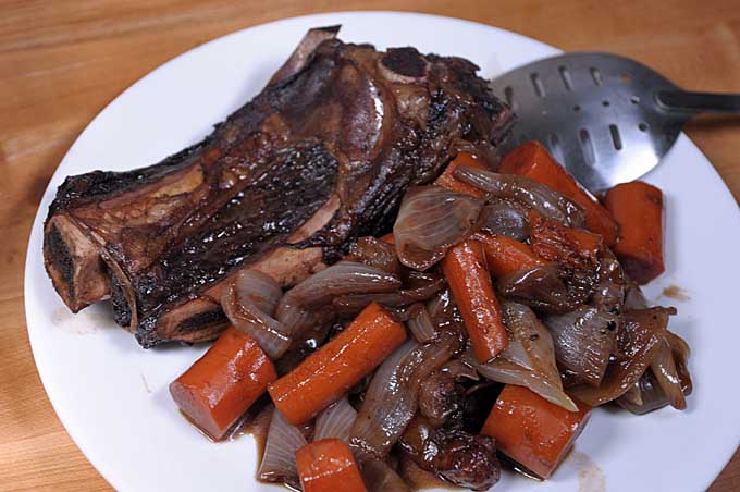 A white ceramic plat with the carrots, onions, and rib bones that were removed from the Au Jus Sauce | Foodal