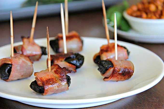 Prunes wrapped in bacon, arranged on a plate and skewered with toothpicks.