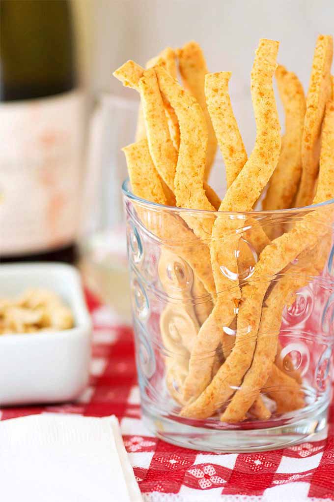 Wavy cheese straws fill a tall patterned glass.
