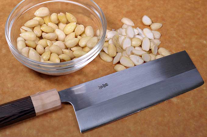 Blanched almonds being cut in a half with a Japanese nakiri knife | Foodal