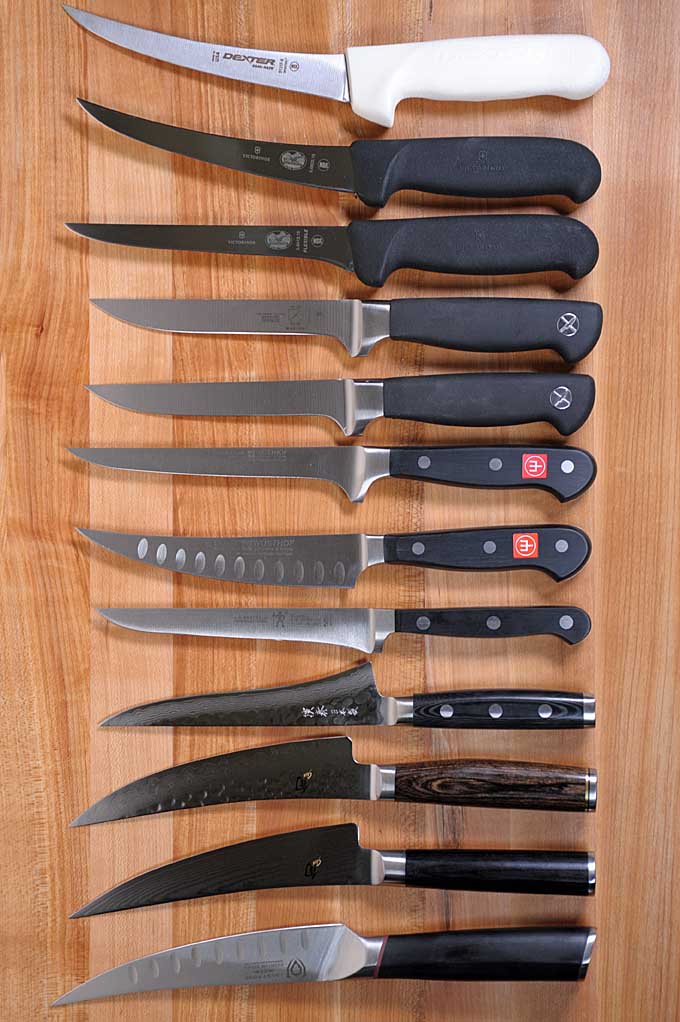 12 different kinds and brands of boning knives and Japanese Gokujos laid out in a row on a maple cutting board | Fooda 
