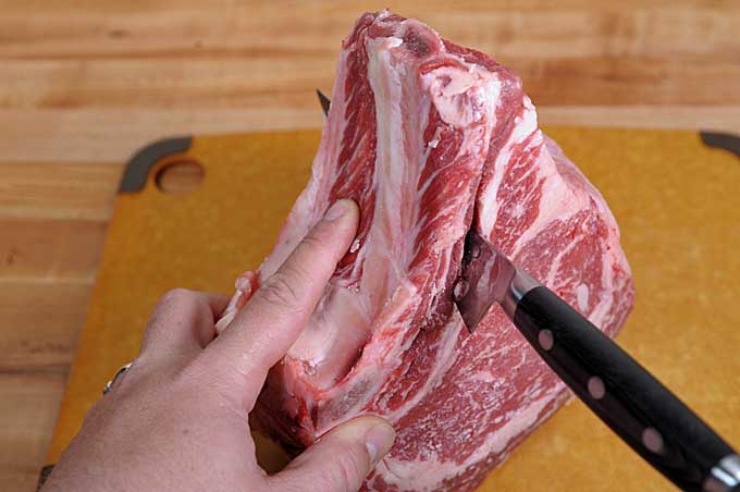 A boning knife cuts downwards to separate the bones from the flesh of the prime rib | Foodal
