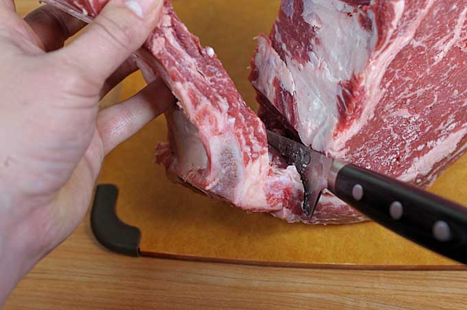 A boning knife being use to cut around the top rib in a standing rib roast | Foodal
