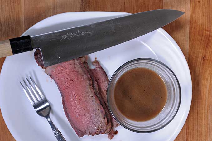 Top down view of a ceramic plate with a standing rib roast and a round glass serving dish full of au jus sauce | Foodal