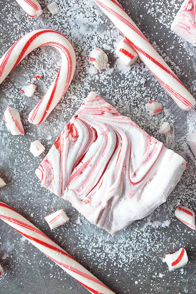 Top down view of candy canes and peppermint pieces and homemade marshmallows on a gray slate counter-top.