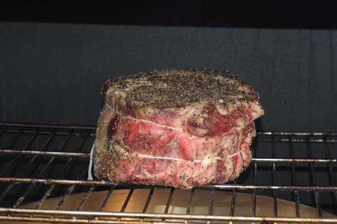 A standing rib roast in a smoker with a pan underneath to catch juices | Foodal
