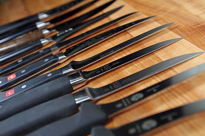 Close up of 12 different boning knives on a maple cutting board diffused focus | Foodal
