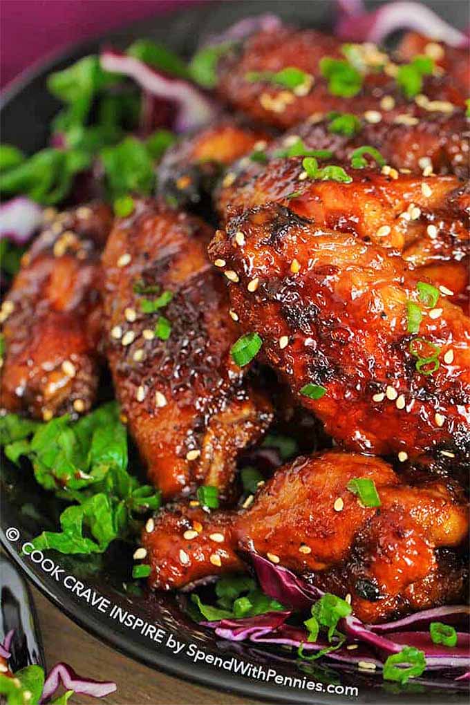 Closeup of chicken wings coated in a sticky glaze and sprinkled with fresh herbs and sesame seeds.