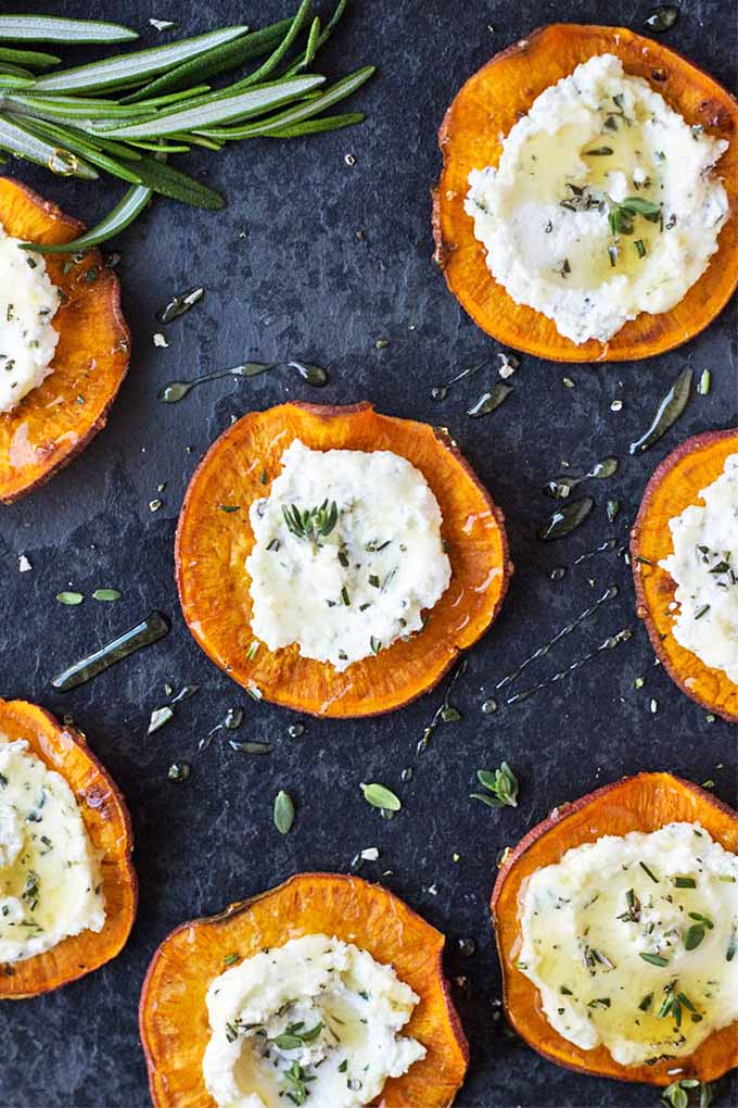 Overhead image of sweet potato rounds topped with a creamy spread and herbs, on a slate surface.