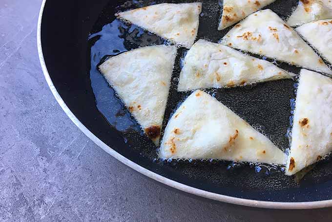 Starting to Fry Triangles of Tortilla Wraps in a Pan of Oil | Foodal.com