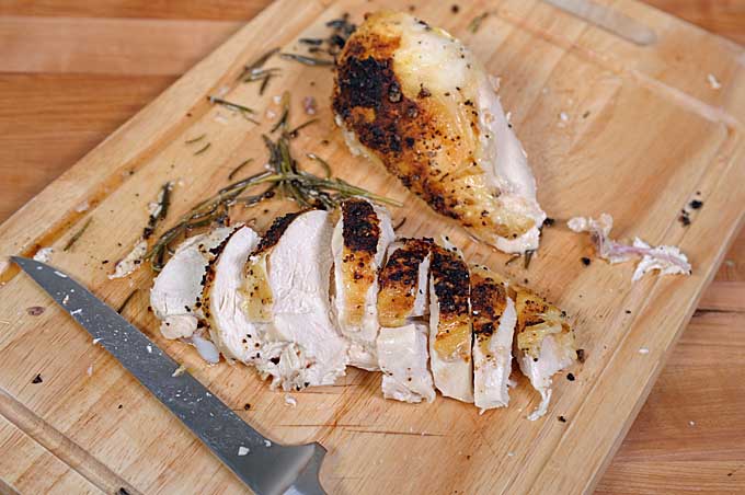Oblique view of a lemon roasted chicken breast being sliced across the grain with a boning knife | Foodal
