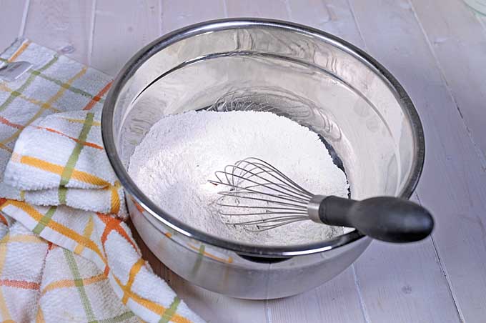The dry ingredients are being mixed with a balloon whisk in a large stainless steel mixing bowl | Foodal 