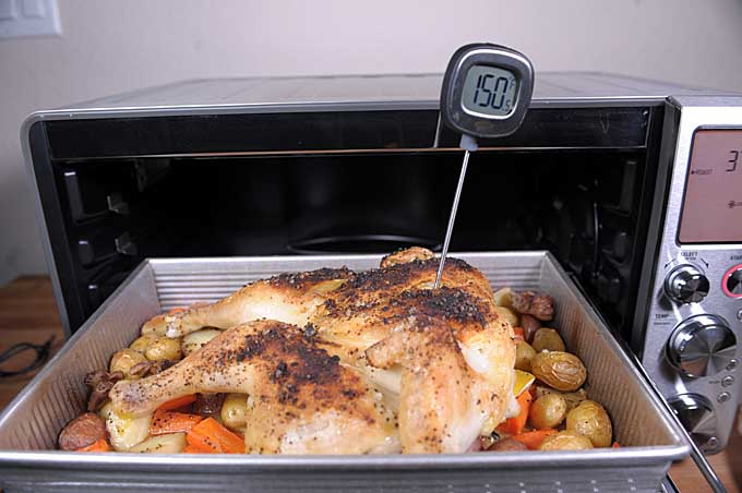 The roasted chicken is being removed from the Breville Smart Oven Air. A meat thermometer reads 150°F | Foodal
