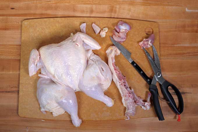 Top view of a raw chicken being spatchcocked and the wishbone removed | Foodal