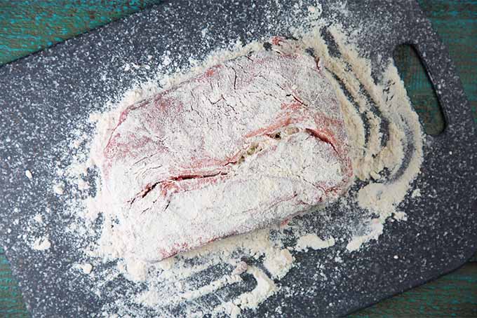 A cut of beef dusted with flour on a black cutting board.
