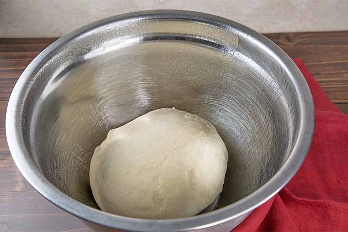 A ball of cinnamon roll dough in a greased stainless steel bowl.