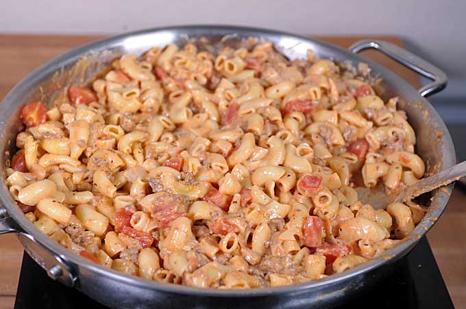 Cooked macaroni noodles being added to the pan and stirred to be covered in sauce. 