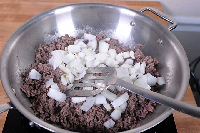 Onions being added to the partially browned hamburger meat inside of the All-Clad Weeknight Skillet.