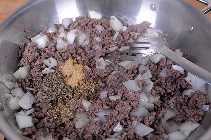 Spices being added to the hamburger and onion mixture.