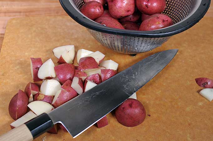 Petite red potatoes being chunked up with a Japanese Gyuto Chef's Knife on a Epicurean cutting board.