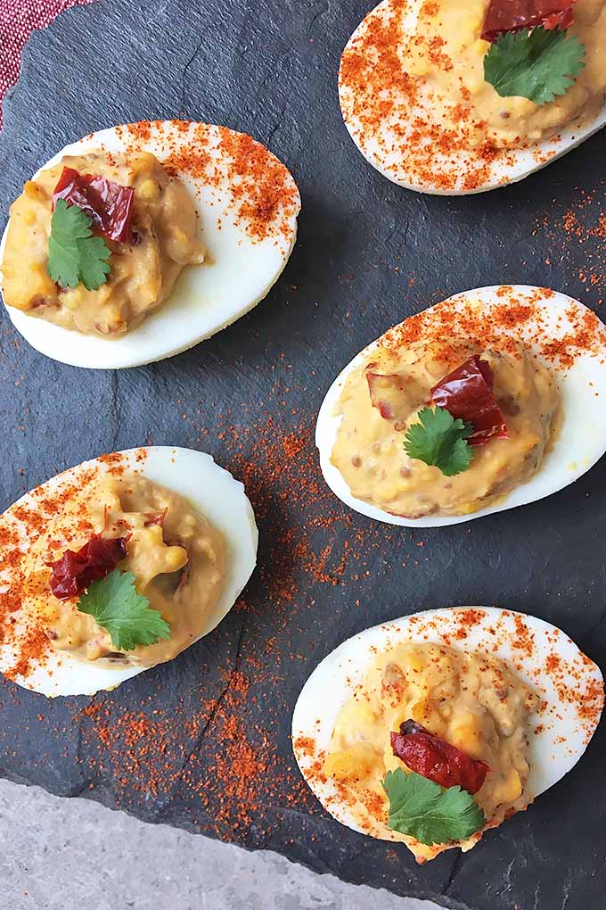 Vertical image of a slate of chipotle deviled eggs with a sprinkle of cayenne
