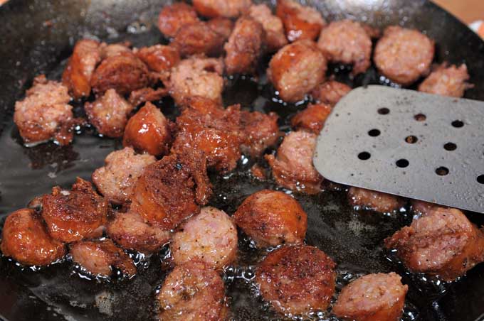 Close up of sausage being browned in a carbon steel frying pan.