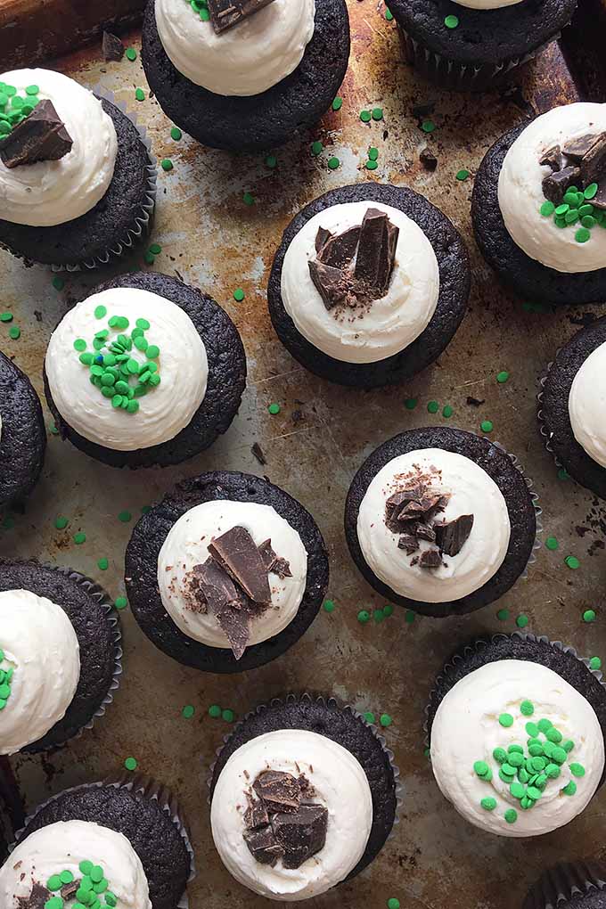 Vertical top-down view of cupcakes with chocolate/green sprinkle garnishes on a cookie sheet. 