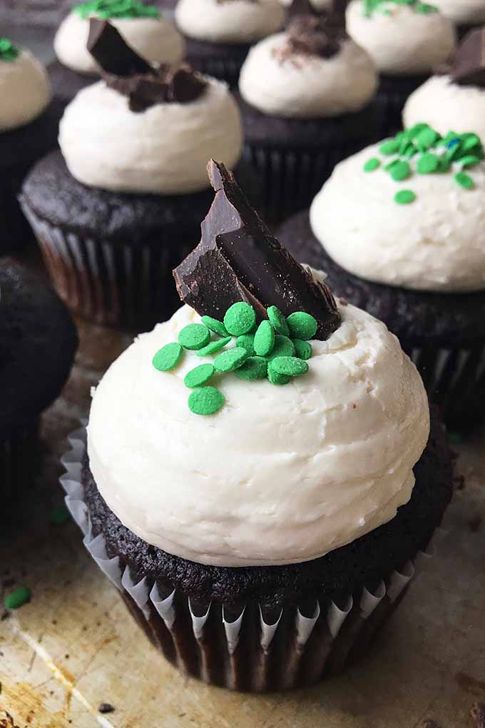 Vertical image of cupcakes with chocolate/green sprinkle garnishes on a cookie sheet. 