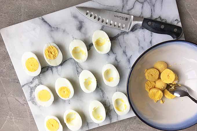 Horizontal image of a knife with egg halves and a bowl of yolks
