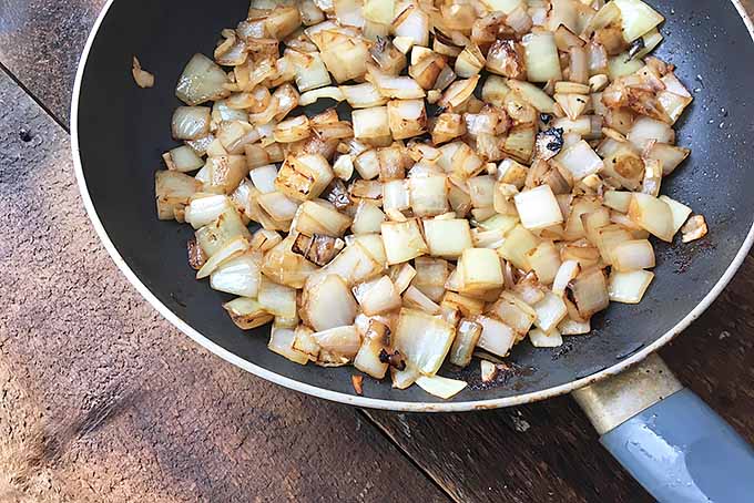 Horizontal image of cooked onions in a skillet on a wooden surface. 
