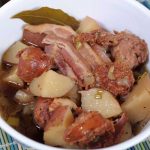 A close up view of an Irish Sausage, Bacon, Potato and Stout Stew in a white porcelain serving bowl.