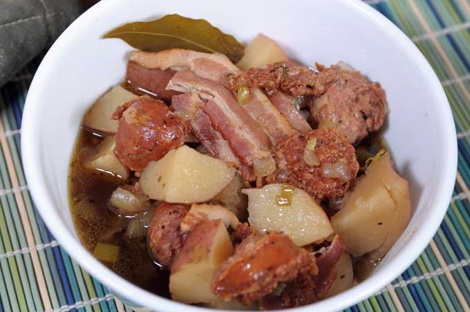 A close up view of an Irish Sausage, Bacon, Potato and Stout Stew in a white porcelain serving bowl.