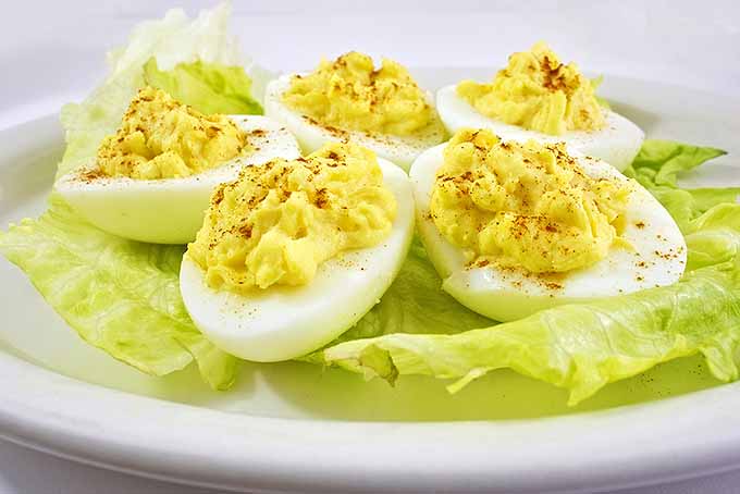 Five deviled eggs topped with paprika and arranged on a large pale yellow-green leaf of lettuce on top of a white plate.