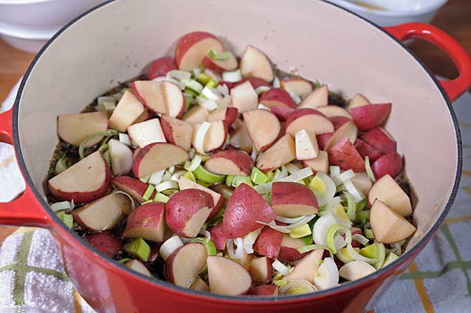 The chunked red potatoes and sliced leek are being layered in over the rest of the ingredients in the red, cast iron Dutch oven.