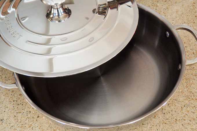 Top view of a stainless steel pan with a lid resting halfway on top of the pan, on a beige counter.