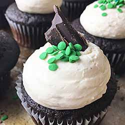 Square image of chocolate cupcakes with chocolate/green sprinkle garnishes on a cookie sheet.