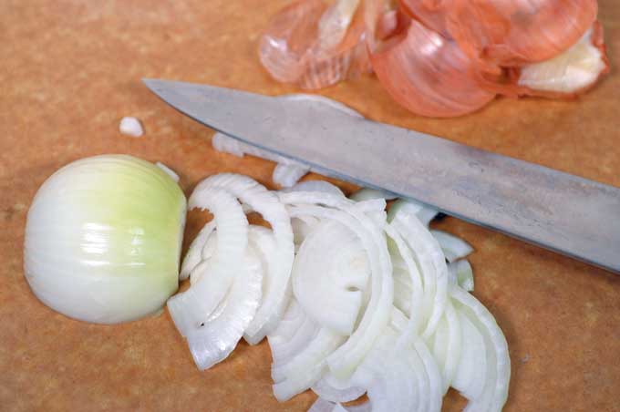 Yellow onion being sliced on a cutting board with a Japanese Gyuto Cook's Knife. 