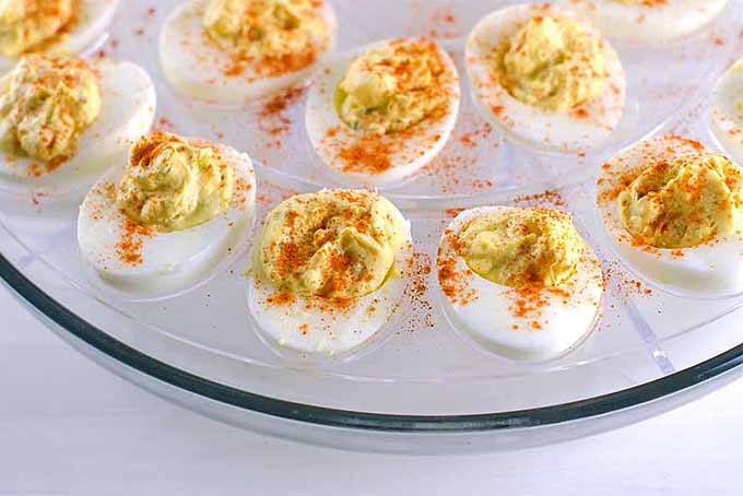 Closeup of deviled eggs topped with paprika and arranged in concentric circles on a glass egg serving plate.