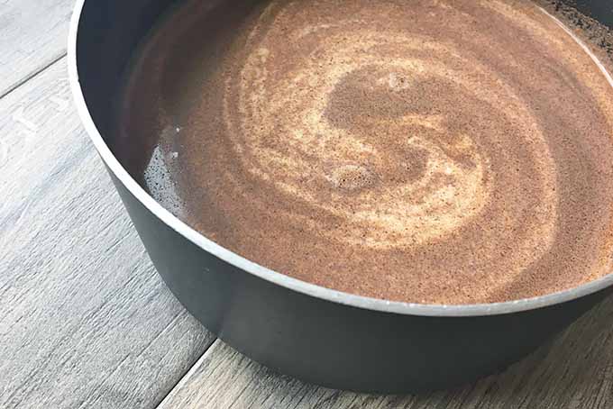 Horizontal image of a spice and milk mixture in a black pot.