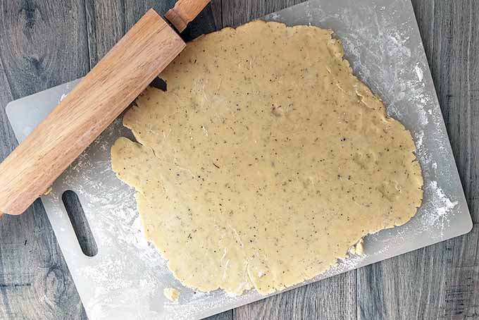 Horizontal image of rolled cookie dough on a cutting board with a rolling pin. 