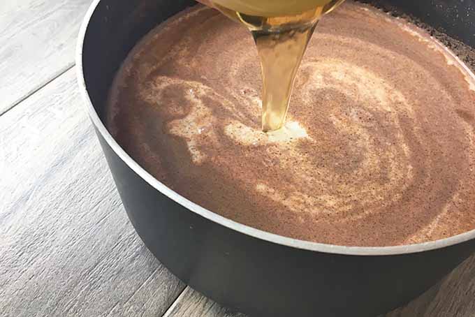 Horizontal image of honey being poured into a spiced mixture in a black pot.