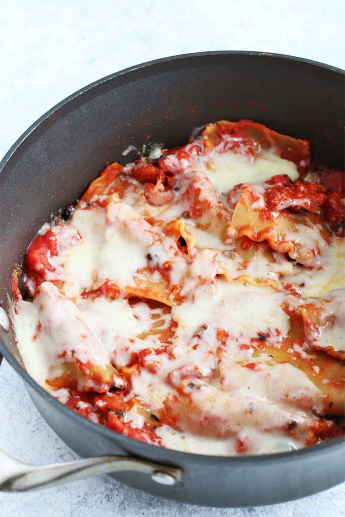 Vertical image of a large nonstick pan filled with no-bake lasagna, topped with melted cheese.