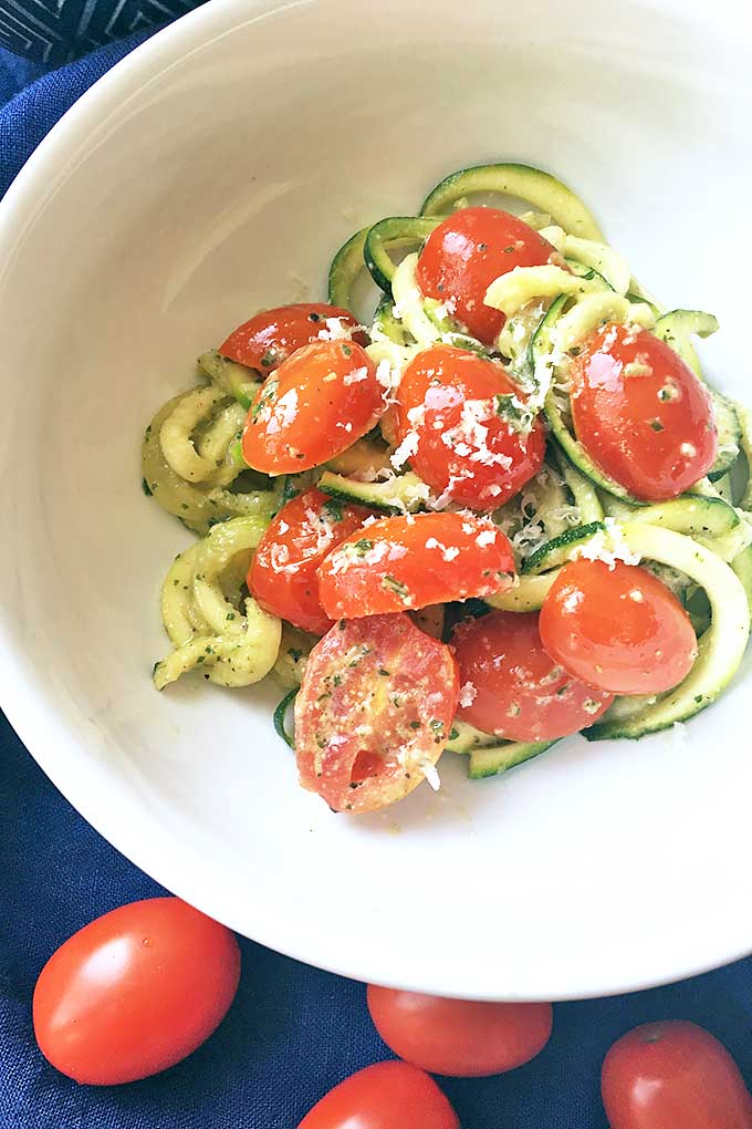 Vertical image of a bowl with spiralized zucchini and tomatoes with grated cheese. 
