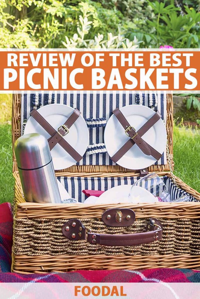 Vertical image of a wicker suitcase-style picnic basket with a handle on the front, fully stocked with dishes, flatware, a metal thermos, and other items, on a red blanket spread out on green grass, with a tree in the background, in bright sunshine, printed with orange and white text near the top and at the bottom of the frame.