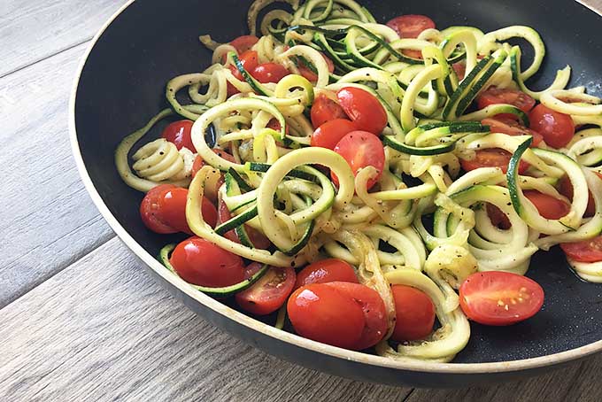 Horizontal image of a pan filled with cooked zucchini and chopped cherry tomatoes. 