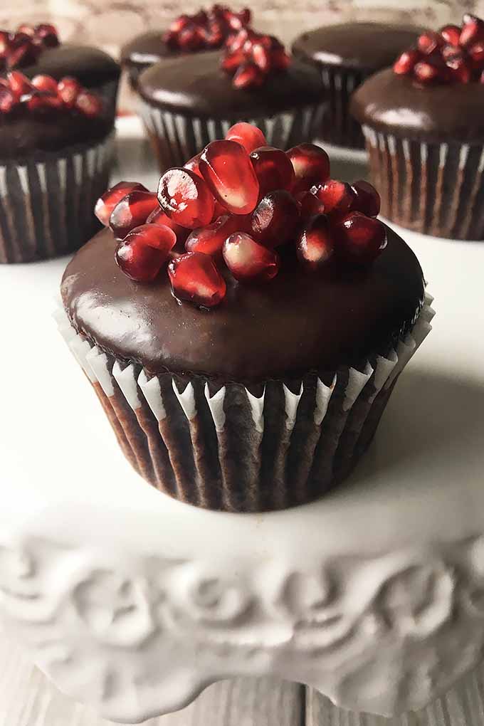 Vertical image of a ganache cupcake with a pile of pomegranate seeds.