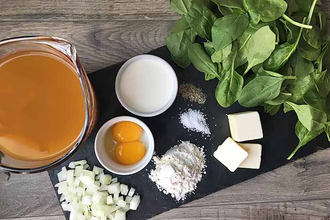 Horizontal image of a slate with ingredients for spinach soup.