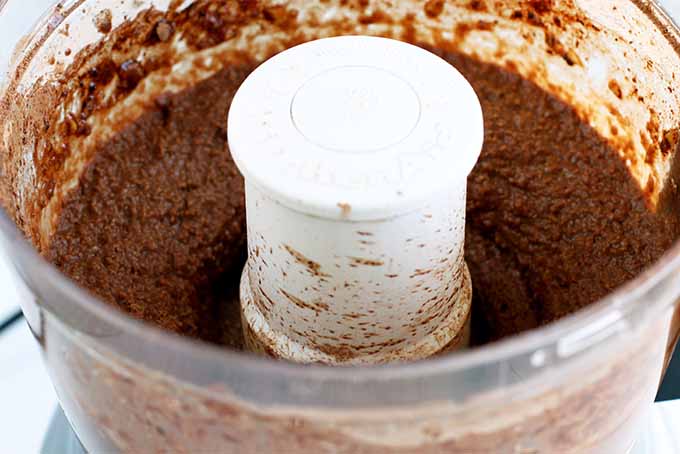 Closeup of a white KitchenAid food processor filled with brown dark chocolate hummus.