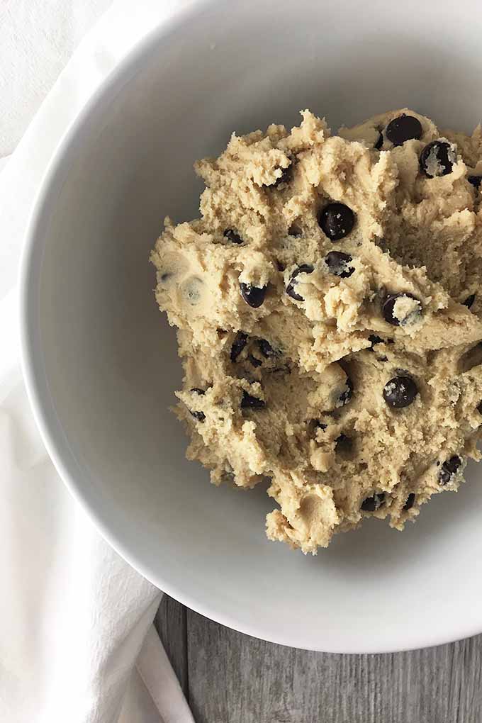 Vertical image of a white bowl filled with chocolate chip cookie dough.