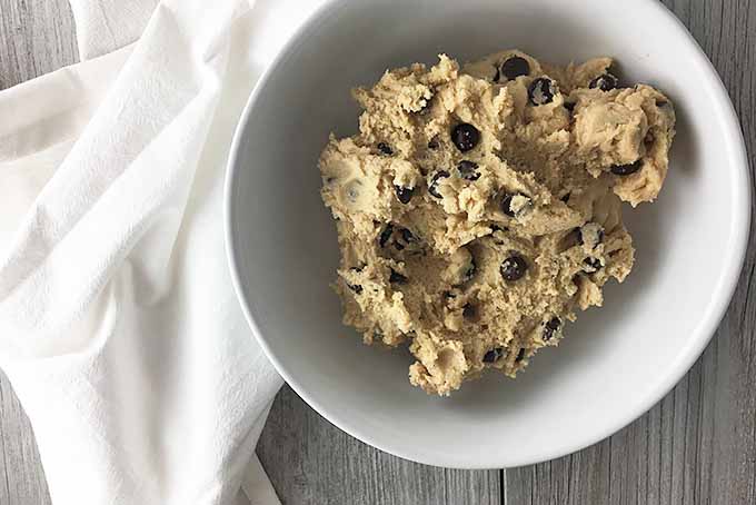 Horizontal image of a white bowl with unbaked chocolate chip cookie dough.